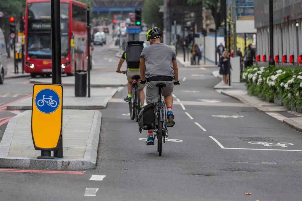 Protected two-way cycletrack on street in London, UK with red double-decker bus in background.